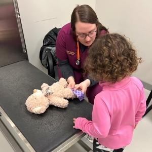 teddy bear being b和aged by vet tech student with child watching